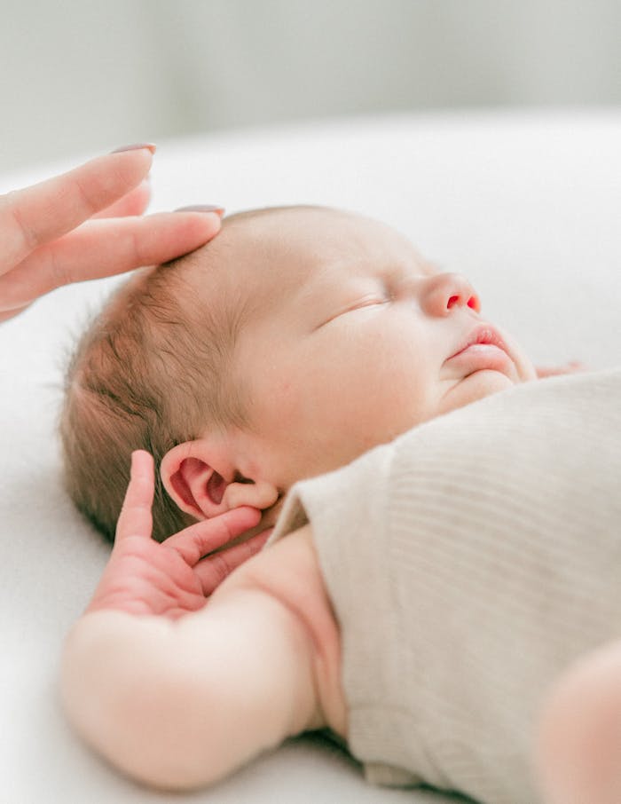 Close-up of a serene newborn baby sleeping, gently touched by hand in soft natural light.